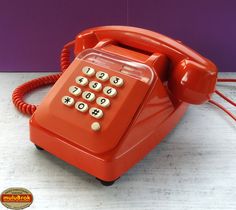 an orange telephone sitting on top of a wooden table next to a purple wall and wires