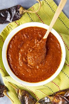 a white bowl filled with sauce on top of a green napkin next to dried peppers