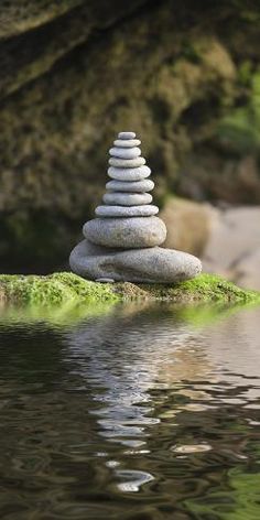 a stack of rocks sitting on top of a green moss covered rock next to a body of water