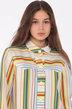 "Vintage 70s shirt in white with rainbow stripes. Buttons down the chest with long sleeves and a collar. Every garment we sell is authentic vintage and one-of-a-kind! You will receive the exact item photographed. Condition: Very good vintage. Best fits women's: Small to medium Material: Feels like Polyester MEASUREMENTS Taken from seam to seam while the garment is lying flat. Double the armpit, waist, and hips For reference, model is 5'5\" and measures 32-24-34. Length from Top: 27\" Armpit to A Retro Long Sleeve Top With Striped Collar, Retro Rainbow Tops For Spring, Retro Spring Top With Rainbow Print, Retro Rainbow Print Top For Spring, Multicolor Button-up Top With Striped Collar, Retro White Long Sleeve Shirt, Vintage White Tops With Striped Collar, Vintage White Top With Striped Collar, Vintage Long Sleeve Tops With Striped Collar