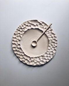 a clock made out of white paper on top of a gray surface with an object in the middle