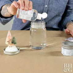 a man is pouring something into a glass jar with a small christmas tree on it