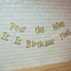 a white brick wall with gold foil lettering on it and some string that says powr the wine is birthday time