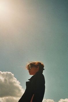 a woman standing on top of a lush green field under a blue sky with clouds