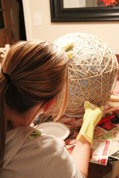 a woman is painting a vase with yellow gloves on her head and holding a paintbrush