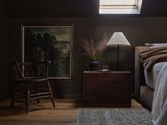 a bedroom with a bed, chair and painting on the wall next to an end table