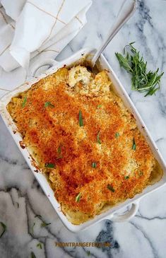 a casserole dish with cheese and herbs in it on a marble countertop