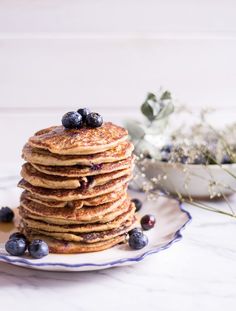 a stack of pancakes with blueberries and syrup on a plate next to some flowers