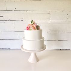 a three tiered white cake with pink flowers on top and greenery in the middle