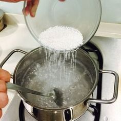 a person pouring water into a pot on top of a stove with food in it