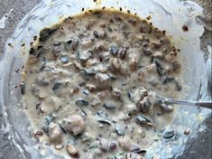 a glass bowl filled with some kind of food on top of a cement ground next to a metal spoon