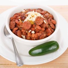 a white bowl filled with chili and cheese next to a green pepper on a plate