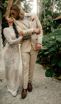 a man and woman standing next to each other in front of some trees with their arms around each other