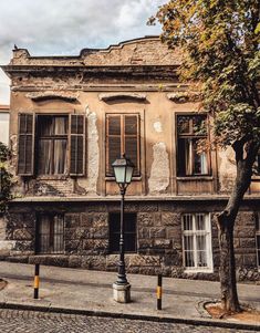 an old stone building with shuttered windows and a lamp post on the sidewalk in front of it