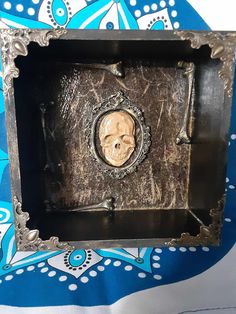 an ornate metal box with a carved skull in the center on a blue and white background