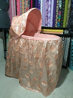 a pink baby bassinet sitting on top of a table in front of colorful fabrics