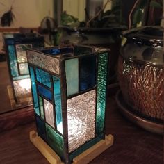 two stained glass candle holders sitting on top of a wooden table next to potted plants