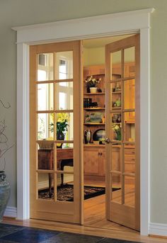 an open wooden door leading to a dining room with glass doors and shelves on either side