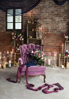 a purple chair sitting in front of a brick wall with candles and flowers on it