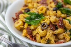 a white bowl filled with pasta and spinach on top of a striped table cloth