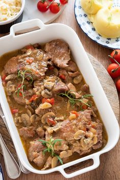 a white casserole dish filled with meat and veggies on a wooden table