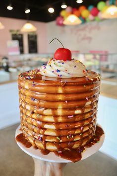 a large stack of pancakes covered in icing and sprinkles with a cherry on top