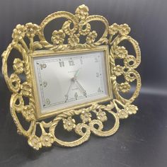 an ornate gold frame with a clock on the front and sides is sitting on a black surface