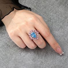 Indulge in the captivating beauty of the pear-shaped fancy blue and pink stone ring. At the center of the ring is a pear-shaped fancy blue stone, radiating with a deep and mesmerizing hue. The blue stone is surrounded by a halo of dazzling pink stones, accentuating its beauty and adding a touch of sparkle. Wearing this remarkable ring is not only a fashion statement but also a celebration of the extraordinary beauty found in nature.Carat Weight: 6.56 ctStone Size: 9*13 mmStone Type: Jeulia® Ston Blue Pear-shaped Diamond Ring For Formal Occasions, Blue Pear-shaped Diamond Jewelry, Luxury Pear-shaped Sapphire Ring With Accent Stones, Pear-shaped Sapphire Jewelry With 17 Jewels, Blue Pear-shaped Fine Jewelry Rings, Pink Stone Rings, Pear Cut, Pink Stone, Blue Stone