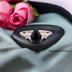 a black diamond ring sitting on top of a pillow next to pink roses and a rose