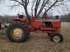 an old red farmall tractor parked in the middle of a field next to a tree