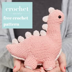 a crocheted pink dinosaur stuffed animal in someone's hands with the text crochet society free crochet pattern