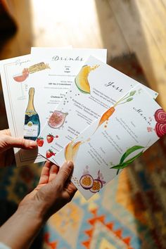 a person holding up some cards with different types of food on them and wine bottles in the background