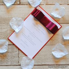 a red ribbon on top of a white card with hearts around it and paper petals