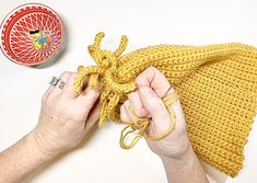 a person is knitting a yellow knitted hat on a white table next to a red object