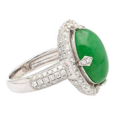 This is part of Chairish’s Fine Jewelry assortment.  Introducing a captivating 18K White Gold Ring, weighing 7.04 grams and adorned with a prong setting for timeless elegance. At the heart of this ring is a vibrant 7.29 carat cabochon-cut "A" grade Jadeite Jade, showcasing a rich green hue. Accentuating the Jade are 126 round-cut Diamonds, totaling 1.19 carats, delicately arranged to enhance the ring's overall brilliance.  Fixed with an intricate milgrain finish around the gemstones.   Item Deta Oval Tsavorite Diamond Ring For Formal Occasions, Elegant White Gold Cabochon Emerald Ring, Elegant White Gold Emerald Cabochon Ring, Timeless Green Diamond Round Ring, Elegant Emerald Jade Ring With Cabochon, Elegant Cabochon Emerald Ring For Formal Occasions, Gia Certified Elegant Oval Cabochon Jewelry, Formal Oval Jade Emerald Ring, Classic Formal Tsavorite Diamond Ring