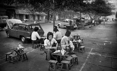 black and white photograph of people sitting at picnic tables on the side of the road