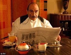 a man sitting at a table reading a newspaper with cups and saucers on it