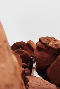 a bride and groom standing on rocks in the desert