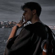 a man standing on top of a boat talking on a cell phone next to the ocean