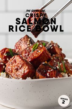 a bowl filled with rice and meat on top of a white table next to chopsticks