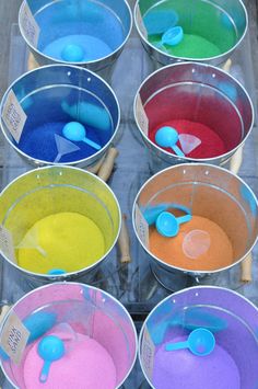 several buckets filled with colored sand and spoons on top of each other in different colors