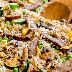 rice and vegetables are mixed together in a skillet with wooden spoons on the side