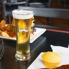 a glass of beer sitting on top of a table next to chips and other food