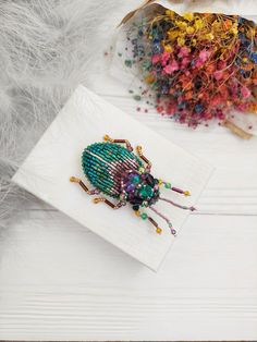 the beaded bug is sitting on top of a white piece of paper next to some feathers