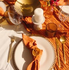 the table is set with orange napkins and silverware, gold utensils