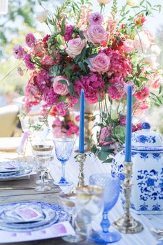 the table is set with blue and white china, pink flowers, and candlesticks