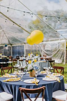 a table set up for a party with yellow balloons and blue cloths on it