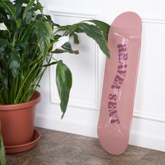 a pink skateboard sitting next to a potted plant