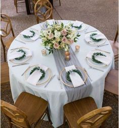 the table is set with white and gold plates, napkins, and greenery