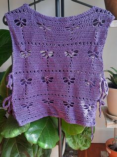 a purple crocheted sweater hanging on a metal rack next to potted plants